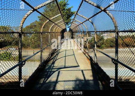 Tunnelansicht einer Fußgängerbrücke, die es Fußgängern ermöglicht, die Autobahn 280 in San Francisco, Kalifornien, USA, zu überqueren; offener Kettenzaun. Stockfoto