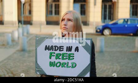 Made in a free world - Slogan auf Protestaktionen in der Stadt. Junge blonde Frau mit Dampfer zu Fuß. Stockfoto