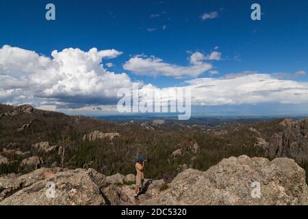 Ein Fotograf steht auf einer Granitfelsen-Formation und fotografiert mit einem dynamischen Landschaftshintergrund im Custer State Park, South Dakota. Stockfoto