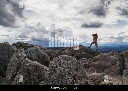 Ein Fotograf steht auf einer Granitfelsen-Formation und fotografiert mit einem dynamischen Landschaftshintergrund im Custer State Park, South Dakota. Stockfoto