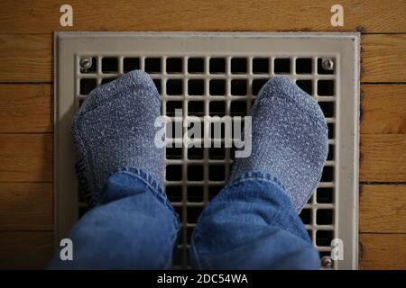 Die Füße des Mannes in Wollsocken, die sich im Winter auf dem Ofengitter eines alten Hauses aufwärmen. Stockfoto