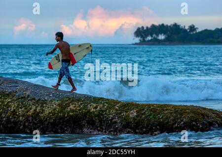 Ein lokaler Surfer bereitet sich darauf vor, am späten Nachmittag in Arugam Bay an der Ostküste Sri Lankas von Eight Star Rock zu springen, um eine Strandpause zu surfen. Stockfoto