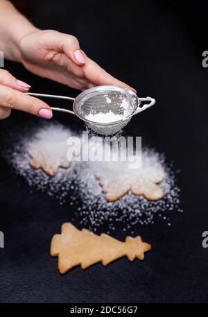 Sieben von Puderzucker oder Mehl auf Keksen. Hausgemachtes Backen Stockfoto