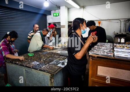 Potenzielle Kunden, einige davon mit Lupe, untersuchen antike buddhistische Amulette in einem Geschäft im Tha Maharaj Pier-Komplex in Bangkok, Thailan. Stockfoto