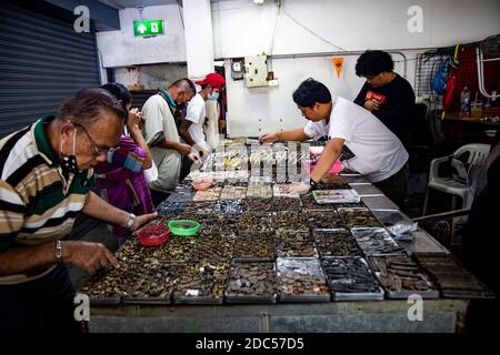 Potenzielle Kunden, einige davon mit Lupe, untersuchen antike buddhistische Amulette in einem Geschäft im Tha Maharaj Pier-Komplex in Bangkok, Thailan. Stockfoto