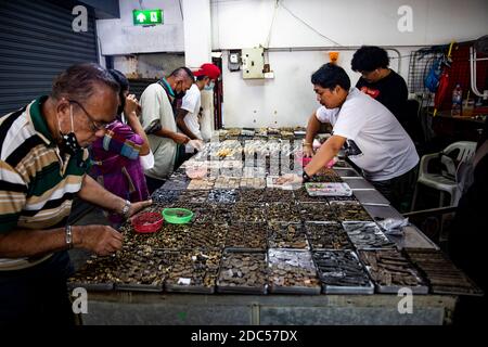 Potenzielle Kunden, einige davon mit Lupe, untersuchen antike buddhistische Amulette in einem Geschäft im Tha Maharaj Pier-Komplex in Bangkok, Thailan. Stockfoto