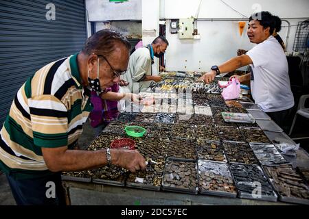 Potenzielle Kunden, einige davon mit Lupe, untersuchen antike buddhistische Amulette in einem Geschäft im Tha Maharaj Pier-Komplex in Bangkok, Thailan. Stockfoto