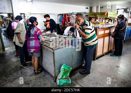 Potenzielle Kunden, einige davon mit Lupe, untersuchen antike buddhistische Amulette in einem Geschäft im Tha Maharaj Pier-Komplex in Bangkok, Thailan. Stockfoto