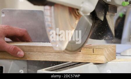 Hand hält ein rohes Holzstück, das von einem schnell schneidenden Kreissägeblatt gesägt wird. Staub ausgeflogen. Industrielle Arbeitsplätze manuelle Berufungsfähigkeiten c Stockfoto