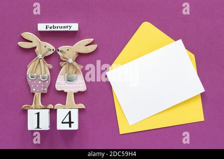 Romantische Komposition Kubenkalender 14. Februar Paar Holzliebhaber Figur Kaninchen, gelber Umschlag mit leerer Karte für Text auf violettem Backgroun Stockfoto