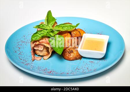 Schweinefleisch in Speck mit gebackenen Kartoffeln auf einem blauen Teller. Stockfoto