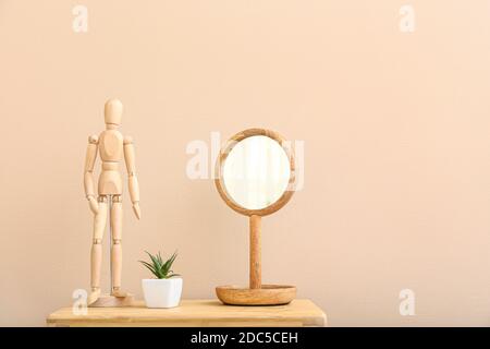 Holzfiguren mit Spiegel und Zimmerpflanze auf dem Tisch im Zimmer Stockfoto