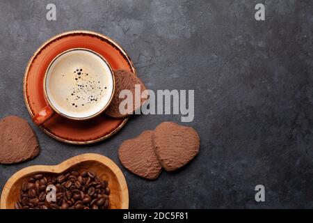 Geröstete Kaffeebohnen in herzförmiger Schüssel, Tasse und Lebkuchen auf Steintisch. Liebe Kaffee Konzept. Draufsicht flach liegend mit Kopierplatz Stockfoto