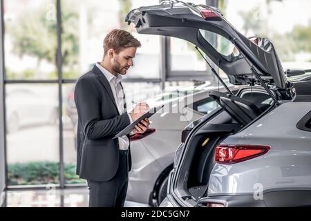 Bärtiger Mann untersucht offenen Kofferraum, Notizen im Showroom Stockfoto