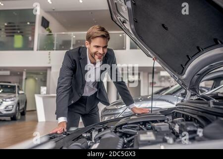 Lächelnder braunhaariger Mann, der offene Autohaube untersucht Stockfoto