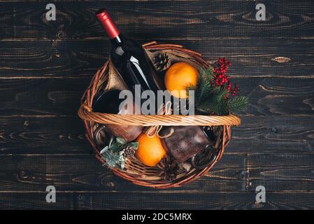 Flasche Rotwein im Weihnachts-Geschenkkorb. Glühwein mit Orangen, Tassen und Tannenbaumschmuck in Box. Draufsicht Stockfoto