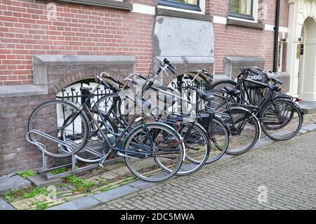 Schwarz-weißes Bild einer Reihe von traditionellen niederländischen Fahrräder mit Ständer und Körbe, geparkt auf einem gepflasterten Straßenbelag. Stockfoto