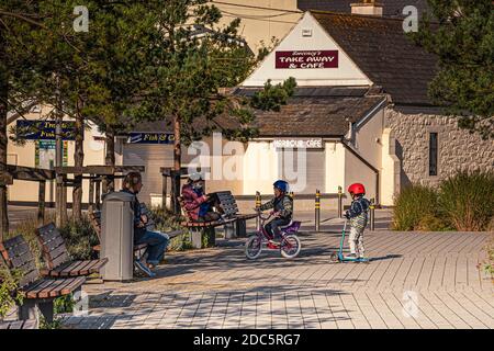 Alltag. Kinder auf dem Fahrrad und Roller im Park. Kinder in sicheren Fahrradhelmen fahren an sonnigen Tagen, während ihre Eltern sie beobachten. Stockfoto