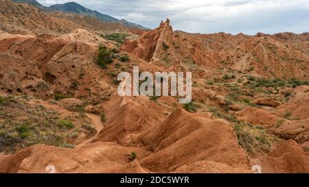 Landschaft des Fairytale Canyon am Issyk kul See in Kirgisistan mit roten Bergen und dunklem Regenhimmel. Stockfoto