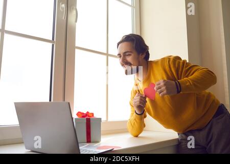 Glücklich junger Mann zeigt Valentine Karte zu seiner Freundin während Videoanruf in Quarantäne Stockfoto