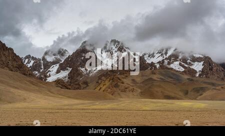 Regen, Wolken und orangefarbene Berge mit Schnee am Pamir Highway in Tadschikistan bei Alichur und Murghab. Stockfoto