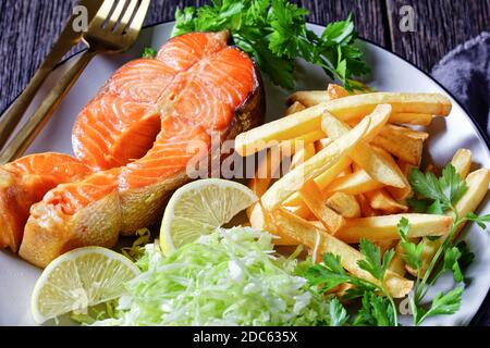 Lachssteaks serviert mit Pommes Frites und Krautsalben auf einem Teller auf einem dunklen Holztisch, horizontale Ansicht von oben Stockfoto