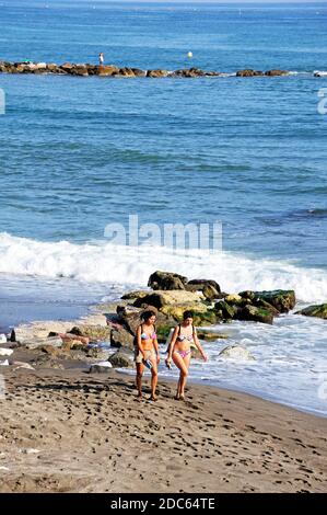 Zwei junge Frauen, die am Strand entlang gehen, Marbella, Spanien. Stockfoto