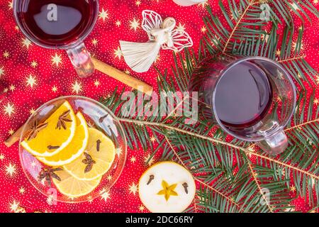 Zwei Tassen heißen Wein oder Gluhwein mit Zimt, Gewürzen und Orangenscheiben auf rotem Weihnachtshintergrund Draufsicht. Traditionelles Getränk im Winterurlaub.Glühwein wi Stockfoto