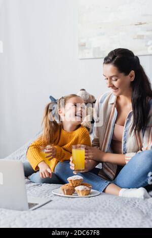 Glückliche Mutter und Tochter, die einander beim Halten anguckend Orangensaft und Filme auf dem Laptop ansehen Stockfoto