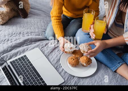 Beschnittene Ansicht von Mutter und Kind halten Orangensaft und Muffins beim Ansehen von Filmen auf dem Laptop Stockfoto