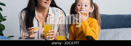 Mädchen essen lecker Muffin in der Nähe lächelnde Mutter hält Orangensaft, Banner Stockfoto