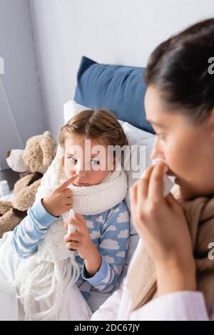 Kranke Mädchen hält Nasenspray in der Nähe Mutter leiden an laufenden Nase auf verschwommenem Vordergrund Stockfoto