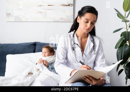Verärgert, erkranktes Kind im Bett liegend in der Nähe des Arztes Schreiben Rezept Stockfoto