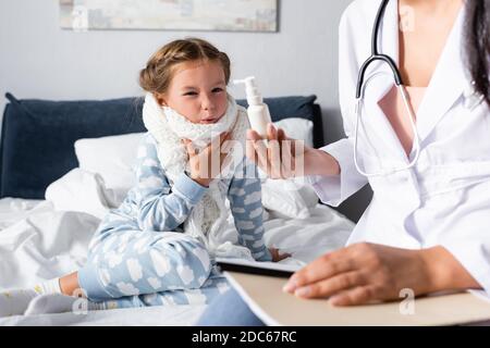 Arzt zeigt Kehlspray zu unzufrieden, kranke Mädchen in warmen Schal um den Hals, verschwommen Vordergrund Stockfoto