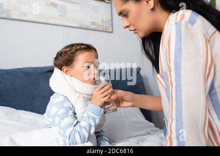 Mutter gibt dem kranken Kind, das darin sitzt, ein Glas Wasser Bett Stockfoto