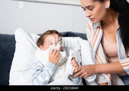Mutter sitzt neben kranken Kind Niesen in Papierservietten in Bett Stockfoto