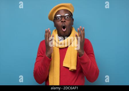 Junger afroamerikanischer Mann mit Brille und Hut, der überrascht aussagt. Studio auf blauer Wand. Stockfoto