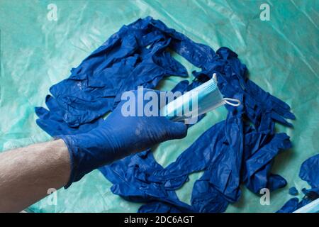 Eine Hand in einem blauen Handschuh mit einer chirurgischen Maske auf einem Stapel von Handschuhen auf einem grünen Sanitärtuch geschützt. Gesundheitsfürsorge und chirurgisches Konzept. Stockfoto