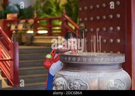 Ein ethnischer indischer Junge legt Joss Sticks in ein Schiff im (chinesisch-Stil) Buddha Tooth Relic Temple and Museum, Chinatown, Singapur Stockfoto