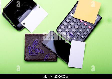 Visitenkarten mit Kopierplatz und Clips mit Aufklebern. Geldbörse, Handy und Lochblende auf grünem Hintergrund. Bürobedarf und Geschäftsidee Konzept. Schreibwaren, Brieftasche, Telefon und Rechner. Stockfoto