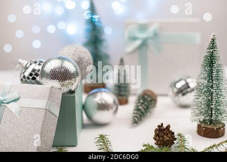 Silberne Weihnachtskugeln in einer Geschenkbox auf einem Hintergrund von Weihnachtsbäumen und blauem Bokeh. Stockfoto