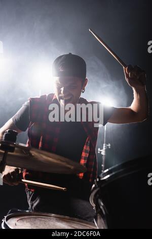 Rockband Drummer hält Drumstick und spielt Schlagzeug mit Rücken Licht und Rauch auf dem Hintergrund Stockfoto