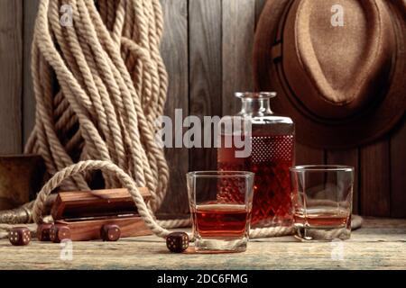 Starker Alkoholiker und Würfel auf einem alten Holztisch. Im Hintergrund sind ein Hanfseil und ein Männerhut. Stockfoto