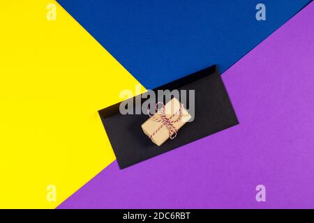 Ein Geschenk in Bastelpapier auf buntem Hintergrund gewickelt. Weihnachten Hintergrund. Minimalkonzept. Flach liegend. Draufsicht. Stockfoto