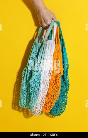 Männliche Hand mit leeren Netztüten auf gelbem Hintergrund. Umweltfreundlicher Zero Waste Bag. Plastikeinkäufe sind kostenlos. Ökologische Sachen für zu Hause. Saitenbeutel Stockfoto