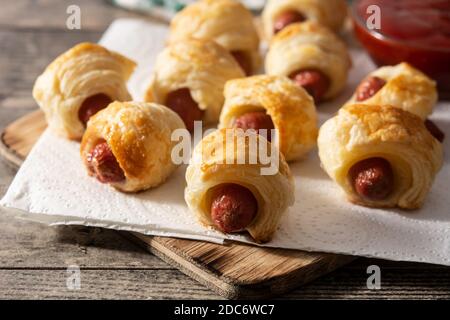 Schweine in Decken. Mini-Würstchen in Blätterteig mit Ketchup-Sauce auf Holztisch eingewickelt Stockfoto