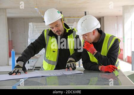 Zwei männliche Bauingenieure diskutieren Zeichnungen auf einer großen Londoner Baustelle. Stockfoto