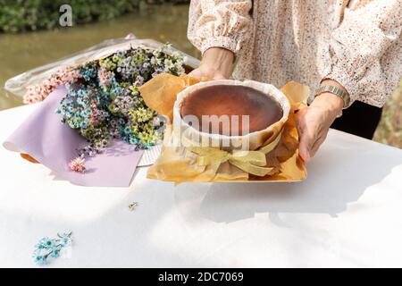 Frau Hände halten Schokoladenkuchen mit Blumenstrauß auf dem Tisch. Stockfoto