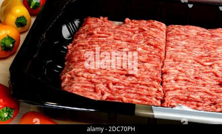 Rohes Hackfleisch in einer Plastikverpackung und buntes Gemüse liegt auf dem Küchentisch. 16x9-Format. Selektiver Fokus. Nahaufnahme. In Innenräumen. Stockfoto