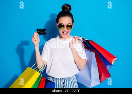 Portrait von positiv schockiert Mädchen genießen Pay-Kauf Kunststoff-Bank Card Hold viele Taschen tragen weiße T-Shirt gestreifte Denim Jeans Isoliert über hell Stockfoto
